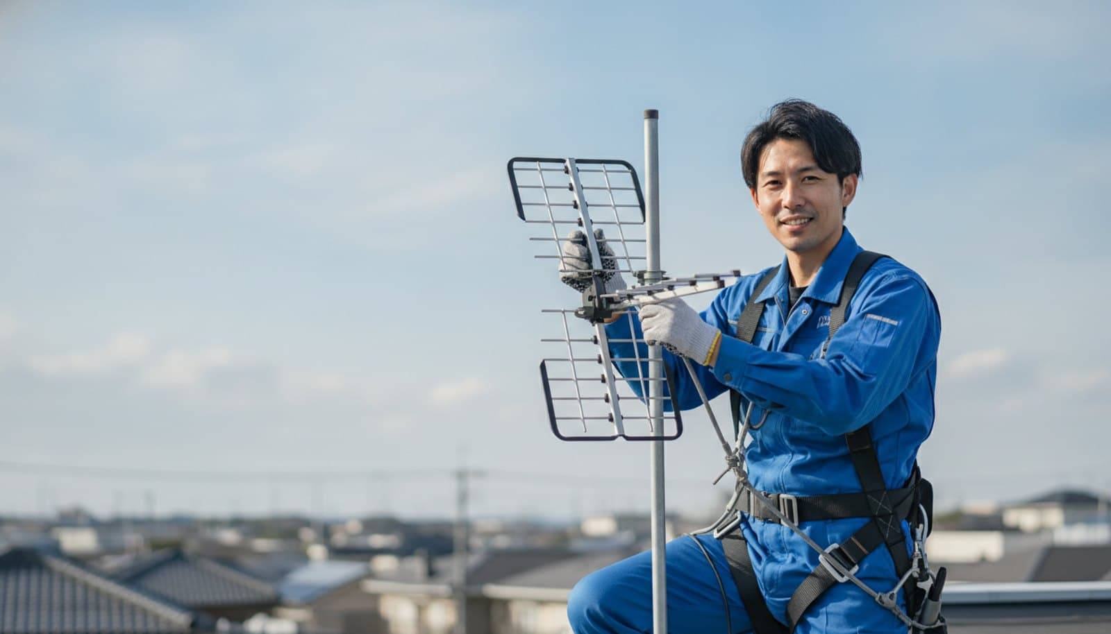 住宅の屋根で、安全帯を着けた技術者が八木式アンテナの向きを調整している